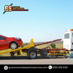 A red car being lifted by a wheel-lift tow truck for transport by Guzman Towing Services in Oakland, CA.