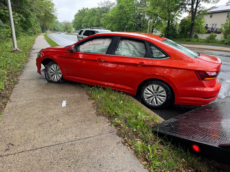A red car with deployed airbags and a flat tire, positioned next to a tow truck bed, indicating a recovery job by Ricky's Towing & Recovery LLC in Derwood, MD.