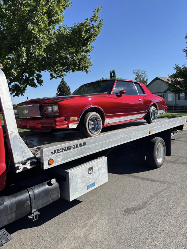 A shiny red classic car being transported on a flatbed tow truck by Luck's Unlimited Towing in Thornton, CO.