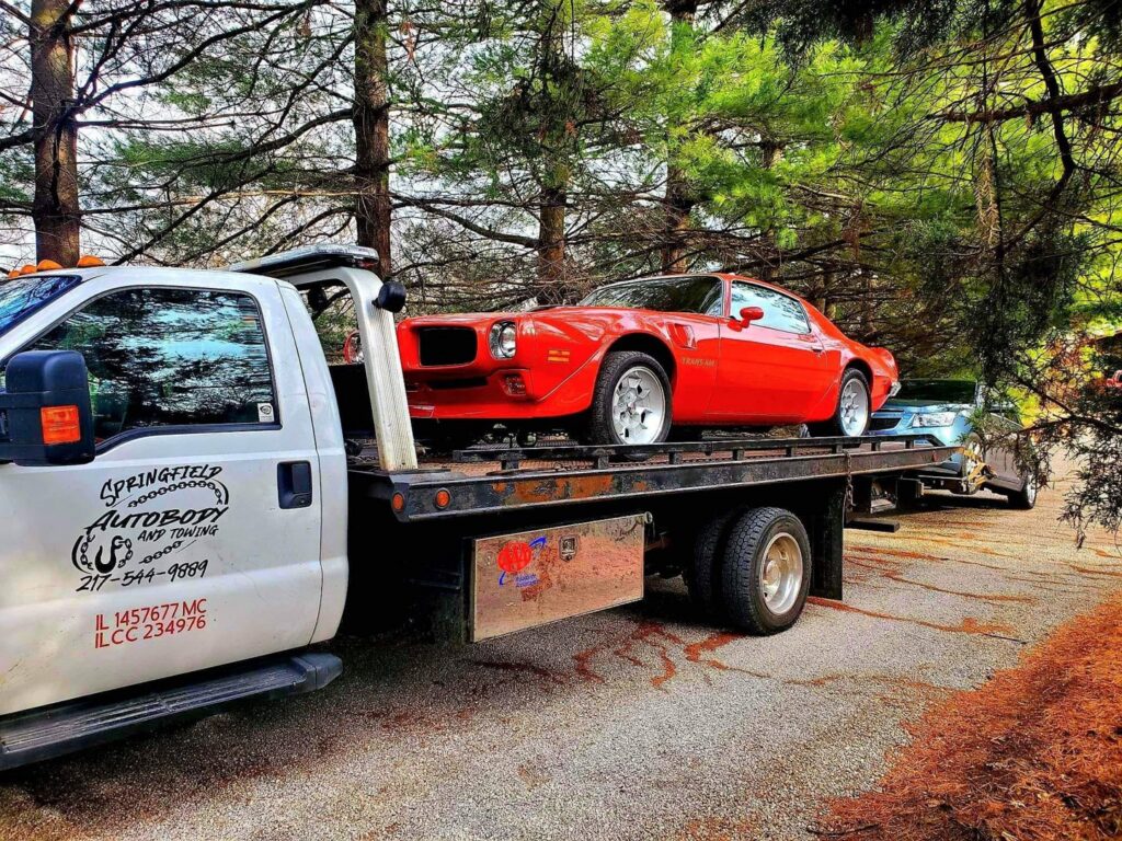 A red classic car being transported on a flatbed tow truck by Springfield Autobody and Towing in Springfield, IL.
