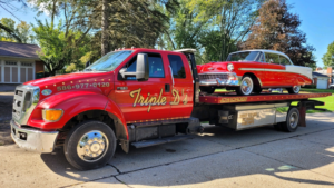 A red and white classic car being transported on a flatbed tow truck by Triple D's Towing in Sterling Heights, MI.