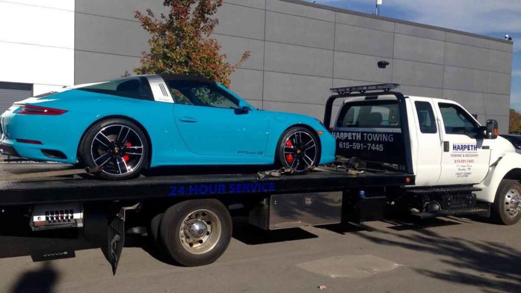 A red classic Corvette being transported on a flatbed tow truck by Harpeth Towing & Recovery in Franklin, TN.