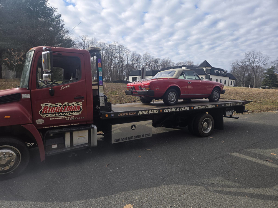 A red convertible sports car being transported on a flatbed tow truck by Riggleman Towing in Moorefield, WV.