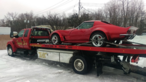 A red classic Corvette being transported on a flatbed tow truck by Triple D's Towing in Sterling Heights, MI.