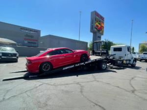 A red Dodge Charger sedan loaded onto a flatbed tow truck by Rojo's Towing in Phoenix, AZ.
