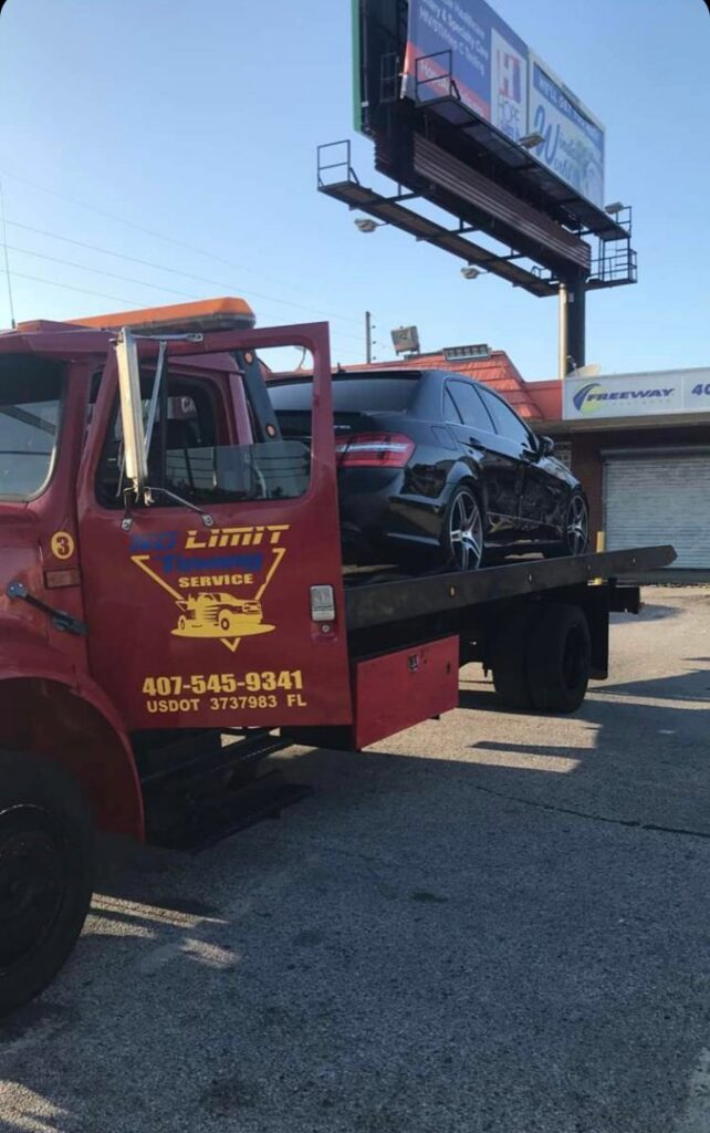 A red flatbed tow truck from No Limit Towing with a black car loaded onto its bed in Orlando, FL.