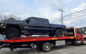 A red flatbed tow truck from Pro-Tech Wrecker Service towing a black pickup truck in Decatur, AL.