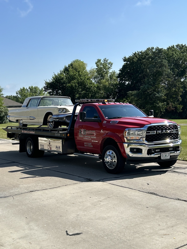 A red flatbed tow truck from A2B Towing & Recovery towing a classic white car in Hazelwood, MO.