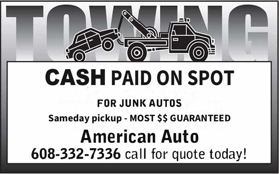 A red flatbed tow truck from American Auto Madison, WI, actively towing a black Mini Cooper on a roadside.