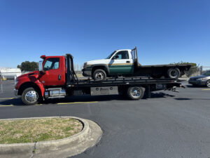 A red flatbed tow truck from Rosco's Towing Services LLC towing a white and green pickup truck in Carencro, LA.