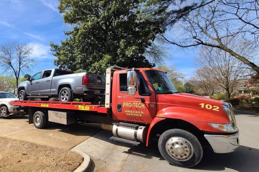 A red flatbed tow truck from Pro-Tech Wrecker Service towing a silver pickup truck in Decatur, AL.
