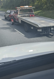 A red flatbed tow truck towing a dark SUV on a highway for RMJ Towing Services in Phoenix, AZ.