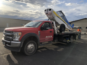 A red flatbed tow truck from AK Car Crushing & Recycling & ACCR Towing transporting a small airplane in Wasilla, AK.