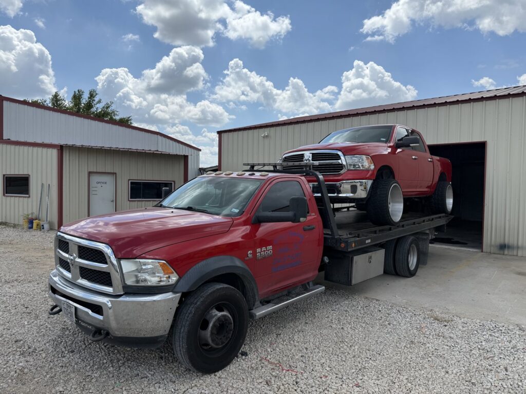A red flatbed tow truck transporting a white, front-damaged sports car for RDZ Towing Service 24/7 in Dallas, TX.
