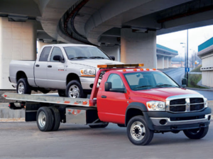 A red flatbed tow truck transporting a silver pickup truck for Towing Services Of Omaha in Omaha, NE.