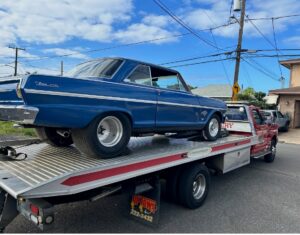A red Tip Tows flatbed tow truck transporting a blue vintage car in Honolulu, HI.