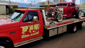 A red Tip Tows flatbed tow truck transporting a red hot rod in Honolulu, HI.