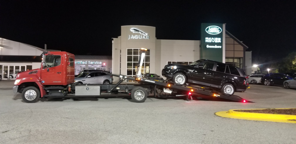 A red flatbed tow truck loading a black SUV at night for RDU Towing & Recovery Services in Raleigh, NC.