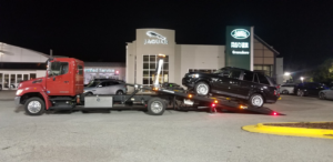 A red flatbed tow truck loading a black SUV at night for RDU Towing & Recovery Services in Raleigh, NC.