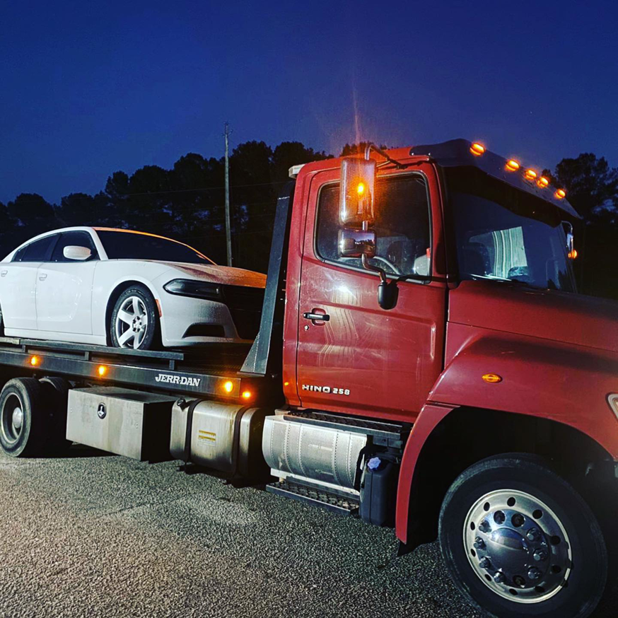 A red flatbed tow truck carrying a white sedan for RDU Towing & Recovery Services in Raleigh, NC.