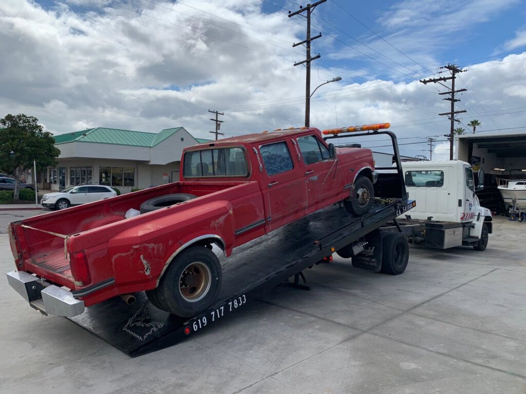 A red Ford dually pickup truck being loaded onto a flatbed tow truck by Cali kings Towing in San Diego, CA.