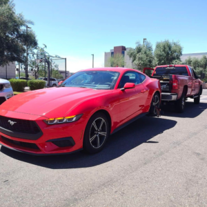 A red Ford Mustang being towed by a red pickup truck, demonstrating towing services by B&E towing and recovery in Mesa, AZ.