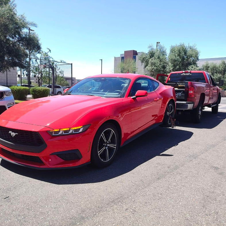A red Ford Mustang being towed by a red pickup truck, demonstrating towing services by B&E towing and recovery in Mesa, AZ.