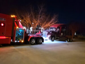 A red heavy-duty wrecker truck preparing to tow a semi-truck at night by Towing Near Me 247 LLC in Irving, TX.