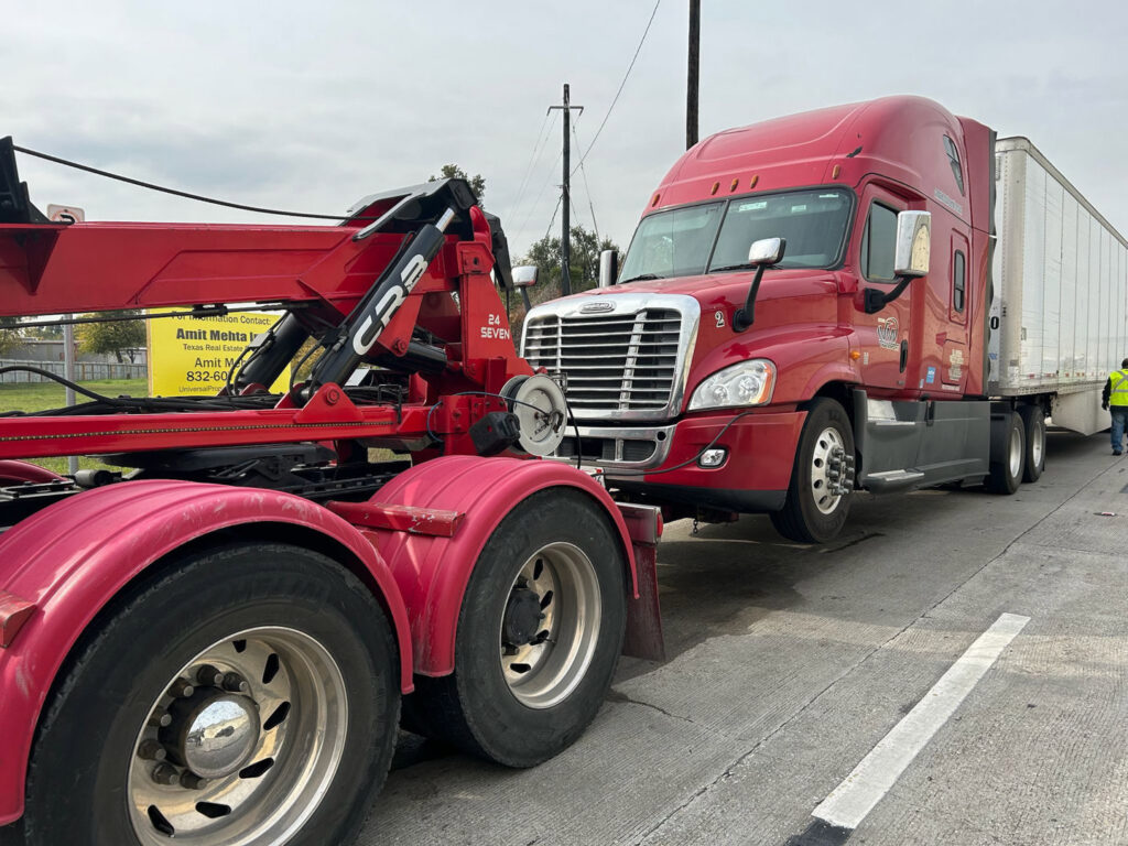 A red heavy-duty wrecker truck towing a semi-truck by Towing Near Me 247 LLC in Irving, TX.