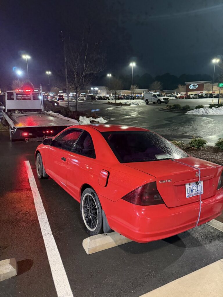 A red Honda Civic coupe with a flat tire being loaded onto a flatbed tow truck by Bullcity Towing & Services LLC in Durham, NC.