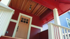A close-up of a house exterior with red horizontal siding and a wooden front door by Lifetime Remodeling Systems in Portland, OR.