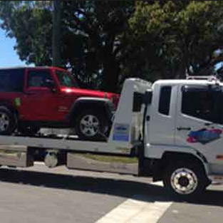 A red Jeep being transported on a white flatbed tow truck by Alexandria VA Towing in Alexandria, VA.