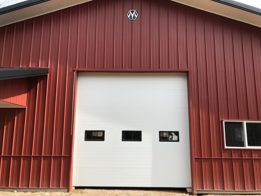 A white industrial garage door with windows installed on a red metal building by Ski Door, Inc. in Center Rutland, VT.