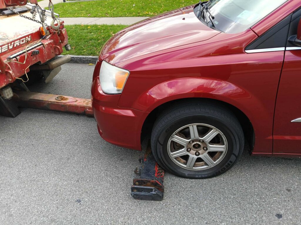 A red minivan being prepared for towing with its front wheels on a tow dolly, handled by Buffalo Towing Services in Buffalo, NY.