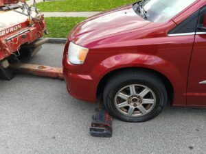 A red minivan being prepared for towing with its front wheels on a tow dolly, handled by Buffalo Towing Services in Buffalo, NY.