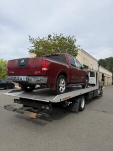 A red Nissan Titan pickup truck loaded onto a flatbed tow truck from Bullcity Towing & Services LLC in Durham, NC.
