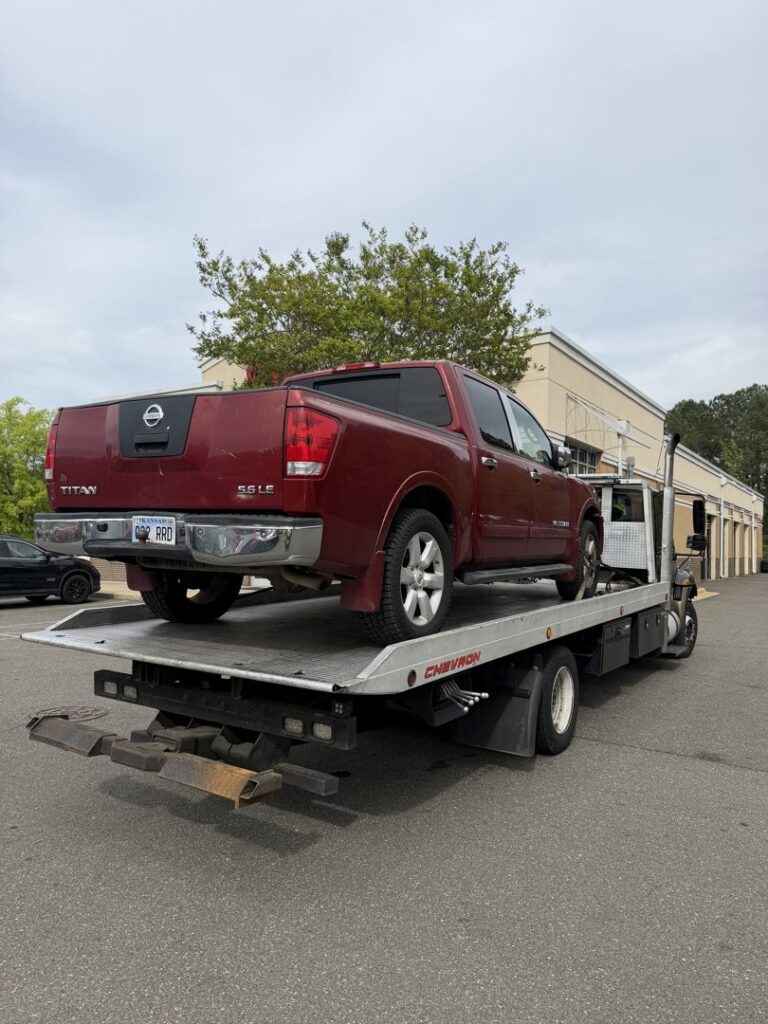 A red Nissan Titan pickup truck loaded onto a flatbed tow truck from Bullcity Towing & Services LLC in Durham, NC.