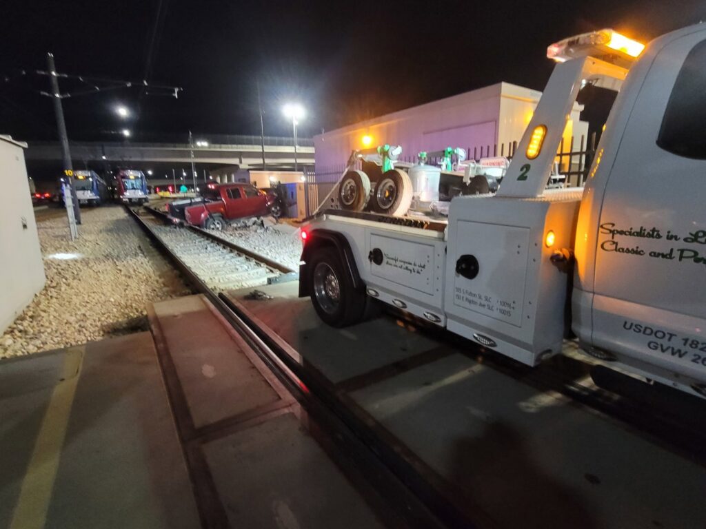 A 4 Wheel Towing truck on scene for a red pickup truck accident recovery near train tracks in South Salt Lake, UT.