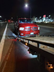 A red pickup truck being loaded onto a flatbed tow truck at night by Classic Towing llc in Greeley, CO.