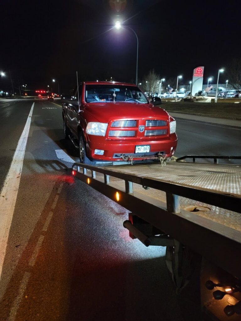 A red pickup truck being loaded onto a flatbed tow truck at night by Classic Towing llc in Greeley, CO.