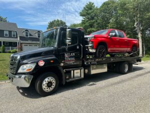 A red pickup truck being transported on a flatbed tow truck by Milan Towing inc. in Milan, MI.