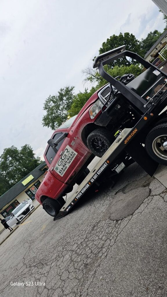A red pickup truck being transported on a flatbed tow truck by Vatos Locos Towing in Cincinnati, OH.