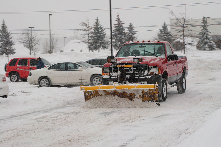 A red pickup truck with a snow plow clearing snow from a parking lot, provided by Green Works Lawn Care in Raleigh, NC.