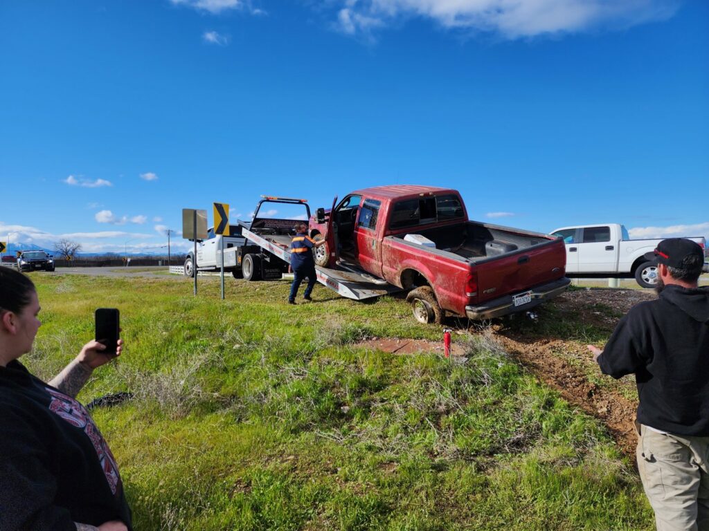 A red pickup truck stuck in mud, being recovered by a white flatbed tow truck from Kennedy Towing & Transport in Anderson, CA.