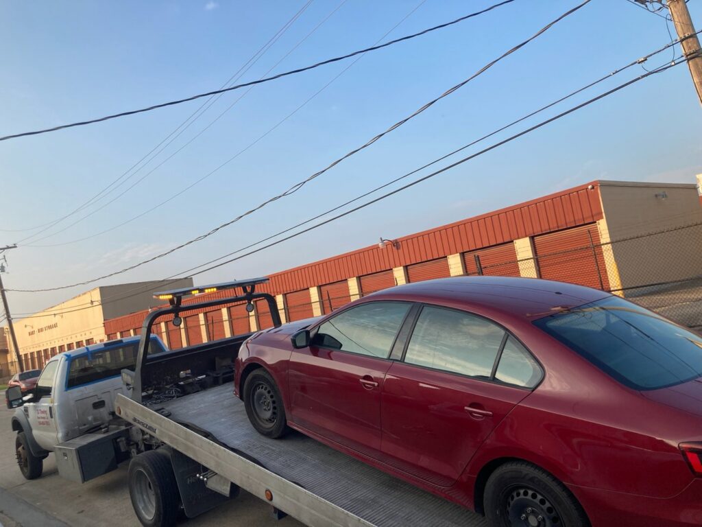 TJ Towing LLC flatbed truck towing a red sedan on a sunny day in New Orleans, LA.