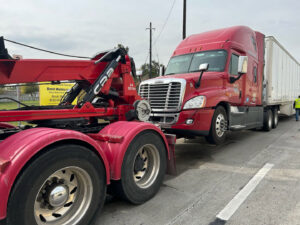 A red semi-truck with a trailer being towed by a heavy-duty tow truck from 247 Towing in San Antonio, TX.