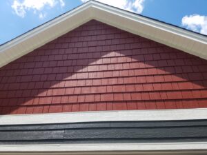 Close-up of a house gable featuring red shake siding above dark gray horizontal siding by Triton Exteriors in Maple Grove, MN.