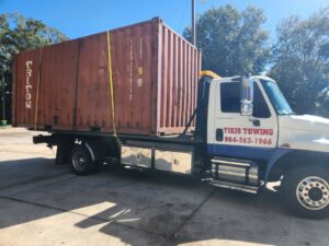A red shipping container being transported on a flatbed tow truck by Tiki's Towing LLC in Jacksonville, FL.