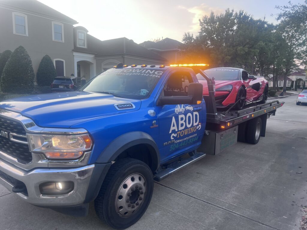 A red sports car being transported on a flatbed tow truck by ABOD Towing LLC in New Orleans, LA, at dusk.