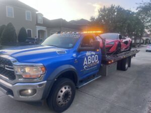 A red sports car being transported on a flatbed tow truck by ABOD Towing LLC in New Orleans, LA, at dusk.